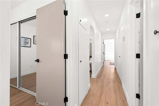 hall with baseboards, recessed lighting, arched walkways, and light wood finished floors
