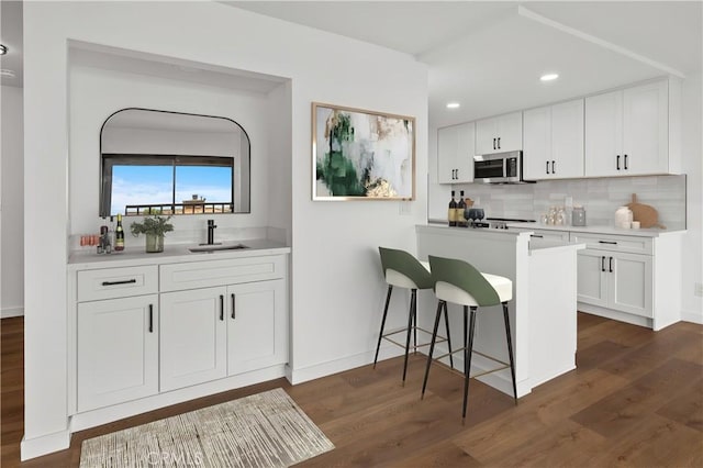 kitchen featuring a sink, stainless steel microwave, tasteful backsplash, white cabinetry, and dark wood-type flooring