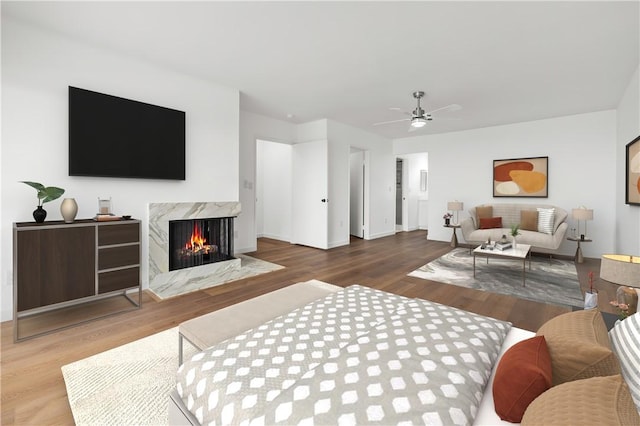 living area featuring a fireplace, wood finished floors, baseboards, and ceiling fan