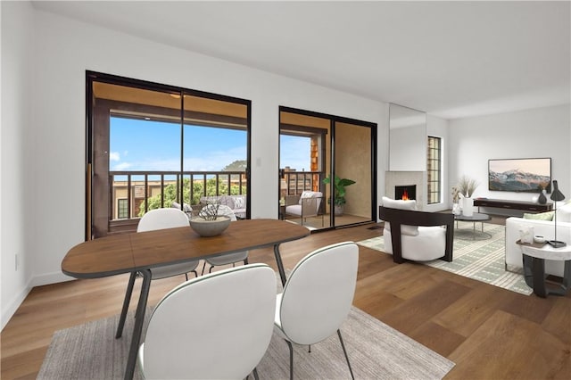 dining room with plenty of natural light, baseboards, a warm lit fireplace, and light wood-style floors