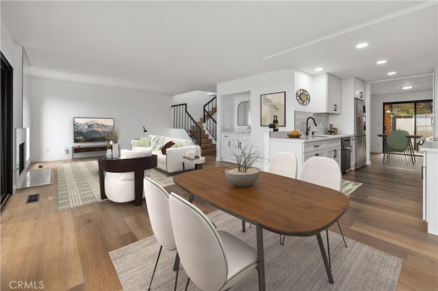 dining area with light wood-style flooring, visible vents, a fireplace, and stairway