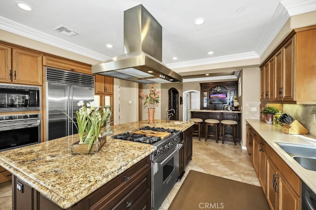 kitchen with built in appliances, island range hood, ornamental molding, and visible vents