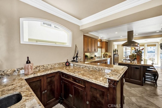 kitchen with light stone countertops, island range hood, a center island, and ornamental molding