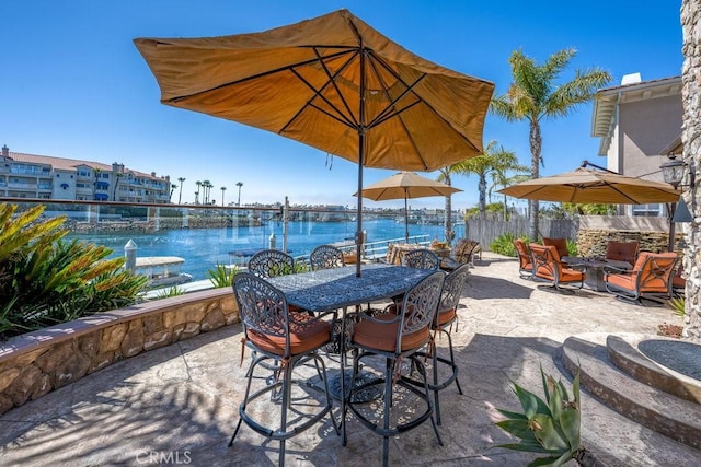 view of patio featuring fence, outdoor dining space, and a water view