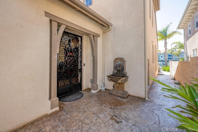 entrance to property featuring a patio, stucco siding, and fence