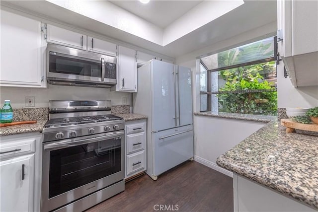 kitchen with white cabinets, baseboards, appliances with stainless steel finishes, dark wood finished floors, and light stone countertops