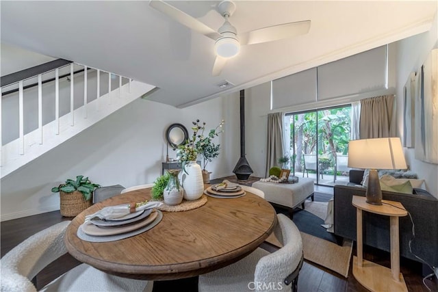 dining space with visible vents, a wood stove, ceiling fan, wood finished floors, and stairs