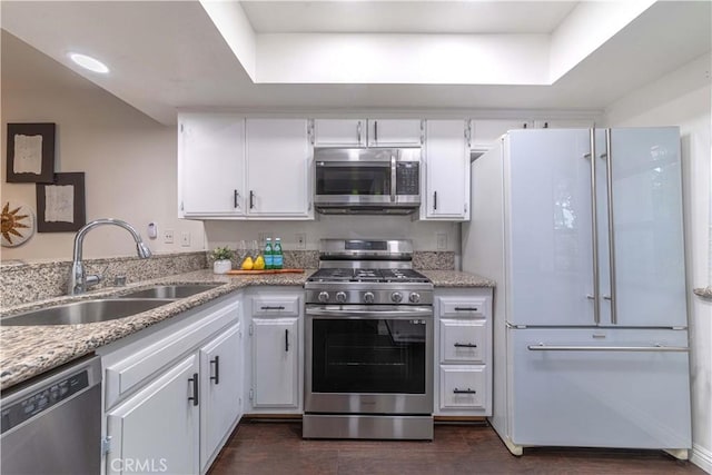 kitchen featuring dark wood-style flooring, light stone counters, white cabinets, appliances with stainless steel finishes, and a sink