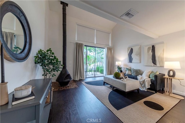 living area featuring visible vents, a wood stove, vaulted ceiling, and dark wood-style floors