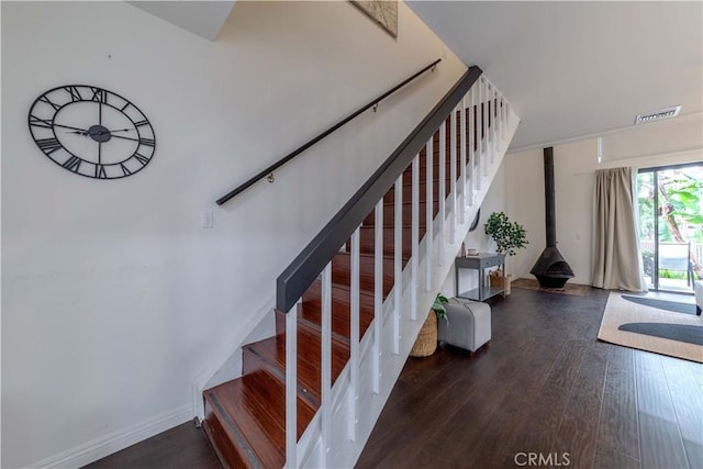 staircase featuring a wood stove, visible vents, and wood finished floors