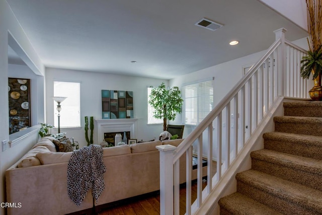 staircase featuring wood finished floors, recessed lighting, a glass covered fireplace, and visible vents