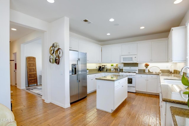 kitchen with a sink, a center island, white appliances, visible vents, and light wood-style floors