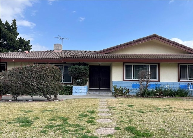 ranch-style home with a chimney, stucco siding, brick siding, a front lawn, and a tiled roof