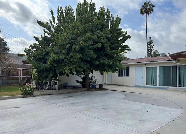 rear view of property featuring a tiled roof, stucco siding, fence, and a patio