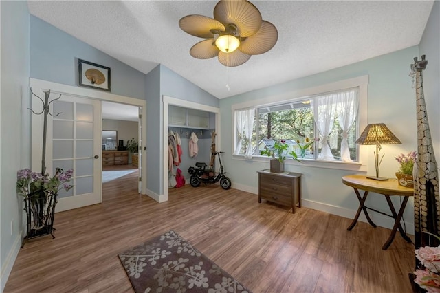 bedroom featuring french doors, a textured ceiling, vaulted ceiling, wood finished floors, and baseboards