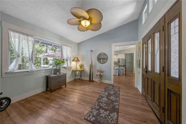 entryway featuring wood finished floors, baseboards, a textured ceiling, a ceiling fan, and vaulted ceiling