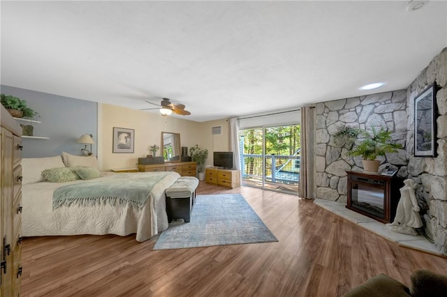 bedroom with visible vents, wood finished floors, a stone fireplace, ceiling fan, and access to outside