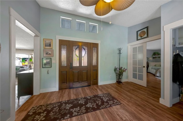 entrance foyer featuring french doors, a textured ceiling, a towering ceiling, wood finished floors, and baseboards