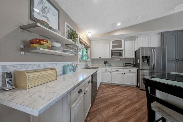 kitchen with a textured ceiling, appliances with stainless steel finishes, open shelves, a sink, and lofted ceiling