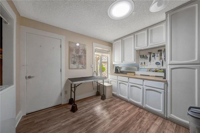 kitchen featuring a textured ceiling, washer / clothes dryer, wood finished floors, light countertops, and baseboards