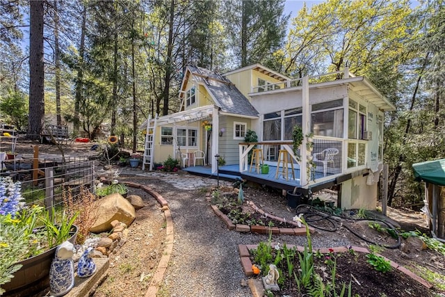 back of house with a shingled roof, a sunroom, and a deck