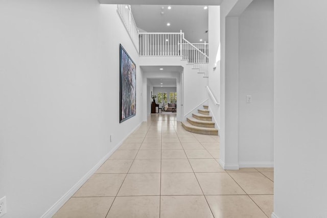 hallway featuring baseboards, stairs, a towering ceiling, and light tile patterned floors