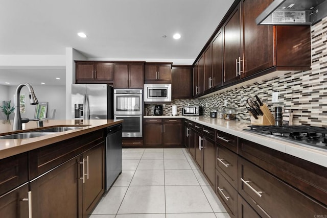 kitchen featuring a sink, decorative backsplash, wall chimney range hood, and appliances with stainless steel finishes