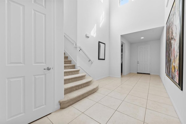 foyer with light tile patterned floors, a towering ceiling, baseboards, and stairway