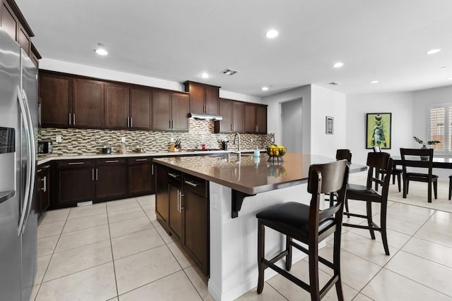 kitchen featuring light tile patterned flooring, backsplash, a kitchen breakfast bar, and appliances with stainless steel finishes