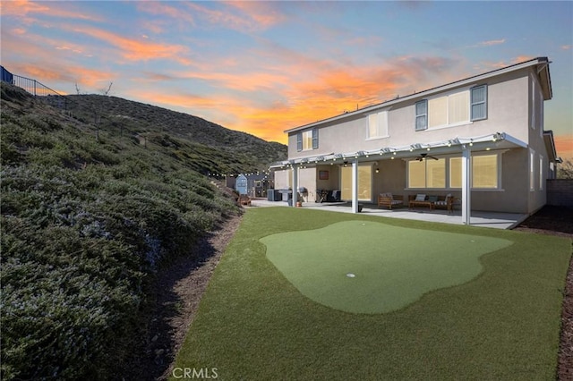 30688 Lone Pine Dr, Menifee, CA 92584 - back of house at dusk featuring a putting green, stucco siding, a patio, and a mountain view