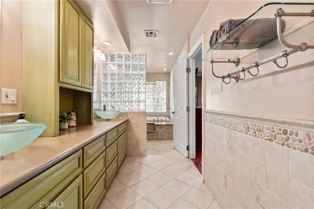 full bathroom featuring tile patterned floors, double vanity, visible vents, a bath, and tile walls
