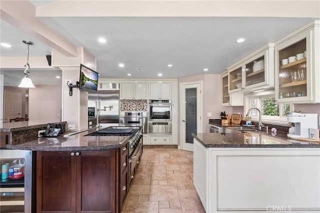 kitchen with stainless steel appliances, stone tile flooring, a sink, dark stone counters, and a warming drawer
