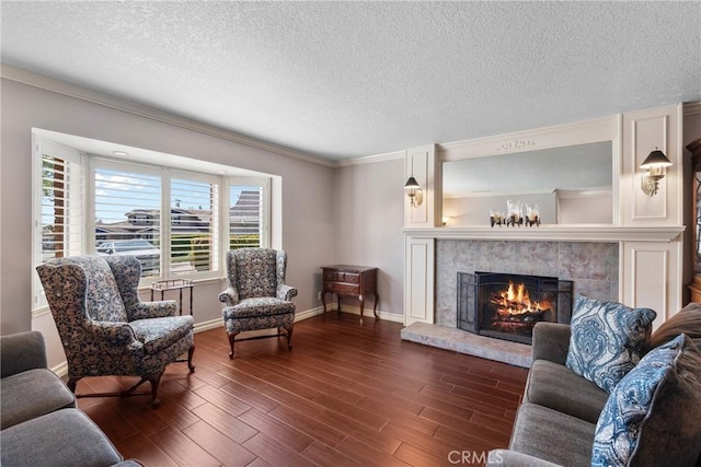 living area featuring a tile fireplace, dark wood-style flooring, a textured ceiling, and crown molding