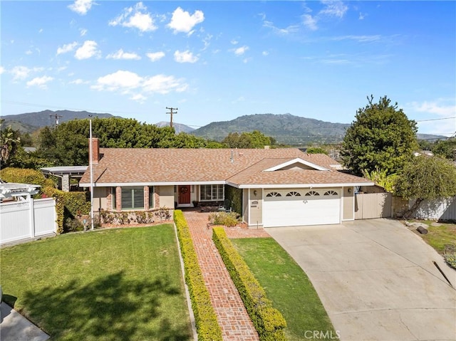 ranch-style home featuring a mountain view, concrete driveway, fence, an attached garage, and a front yard
