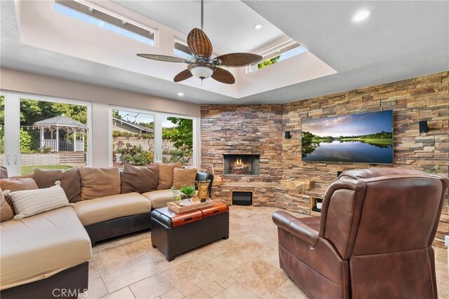 living room featuring a ceiling fan, a tray ceiling, recessed lighting, and a fireplace