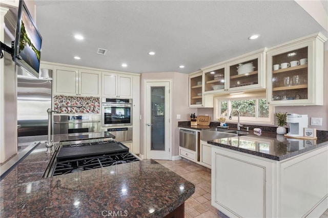 kitchen featuring recessed lighting, dark stone countertops, dishwasher, a sink, and glass insert cabinets