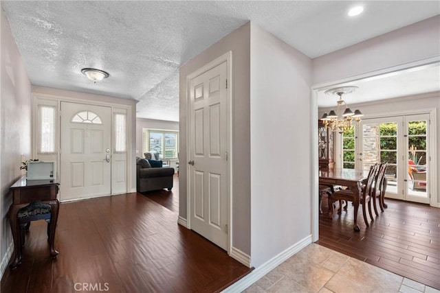 entrance foyer with wood finished floors, a textured ceiling, baseboards, and a notable chandelier