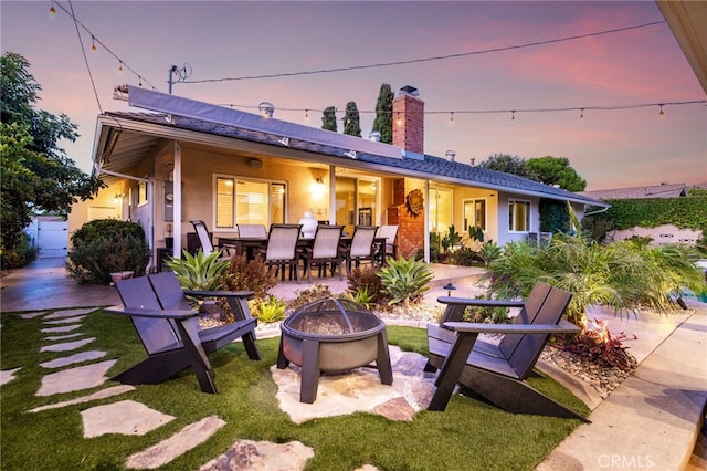 back of house featuring a chimney, outdoor dining area, an outdoor fire pit, a patio, and stucco siding