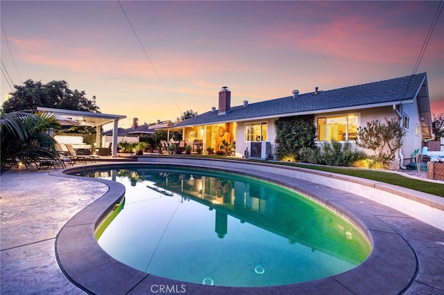 pool at dusk featuring central AC unit, a patio area, and an outdoor pool