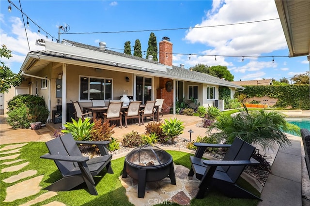 back of property with a fenced in pool, a chimney, an outdoor fire pit, and a patio area