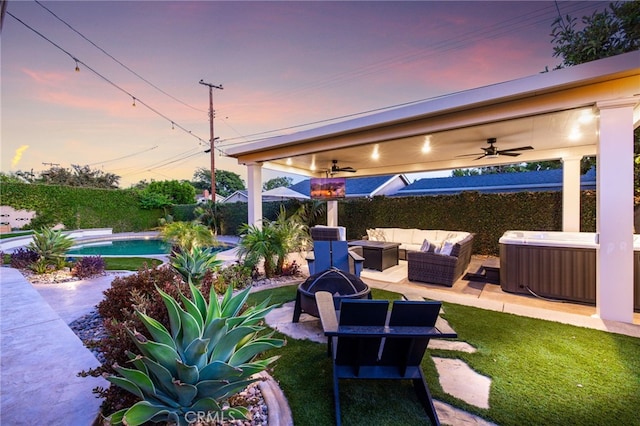 patio terrace at dusk with a ceiling fan, a hot tub, a fenced in pool, a fenced backyard, and an outdoor living space with a fire pit