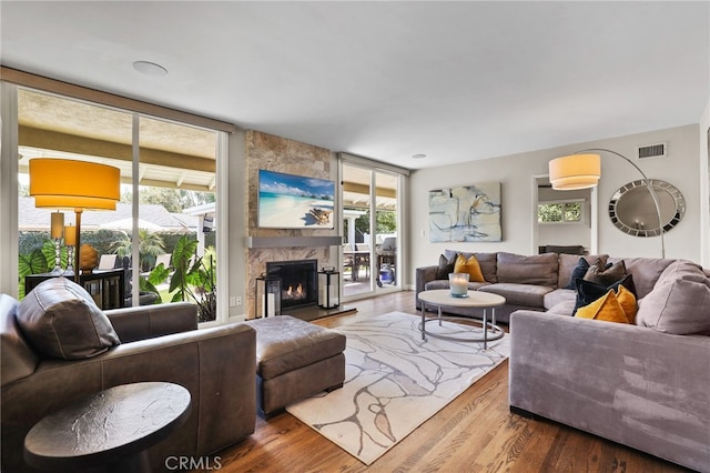 living area featuring a stone fireplace, wood finished floors, and visible vents