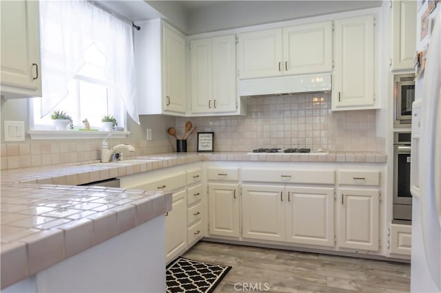 6151 Tyndall Dr, Huntington Beach, CA 92647 - kitchen with tile counters, white cabinets, appliances with stainless steel finishes, and decorative backsplash