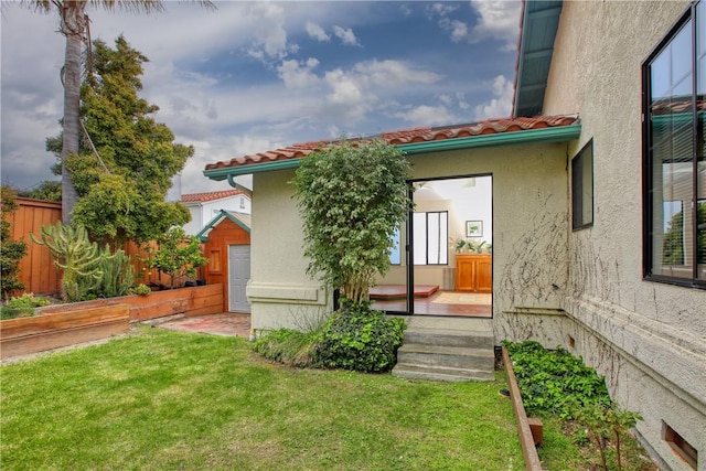 back of property featuring fence, a lawn, a tiled roof, and stucco siding