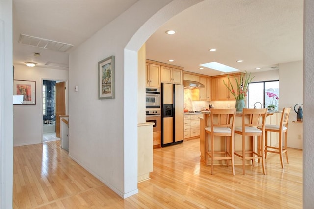 kitchen featuring refrigerator with ice dispenser, light wood-style floors, backsplash, under cabinet range hood, and visible vents