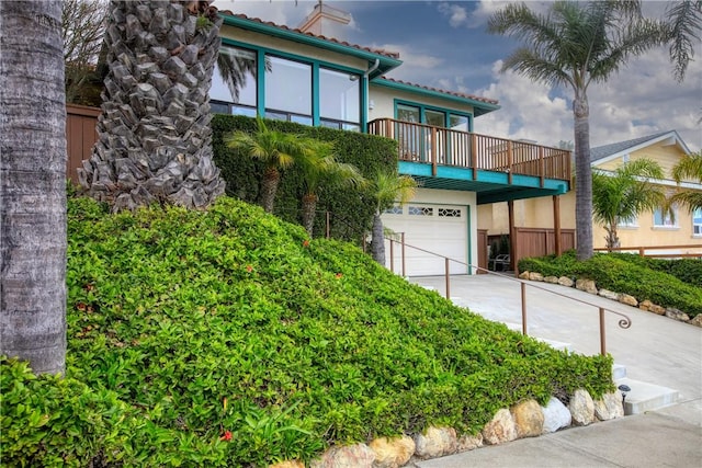 view of front of property featuring a balcony, a chimney, driveway, an attached garage, and stucco siding