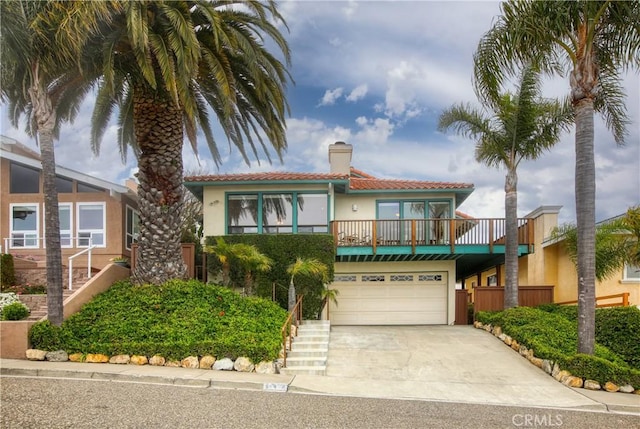 mediterranean / spanish-style house with a balcony, a chimney, concrete driveway, a tiled roof, and stucco siding