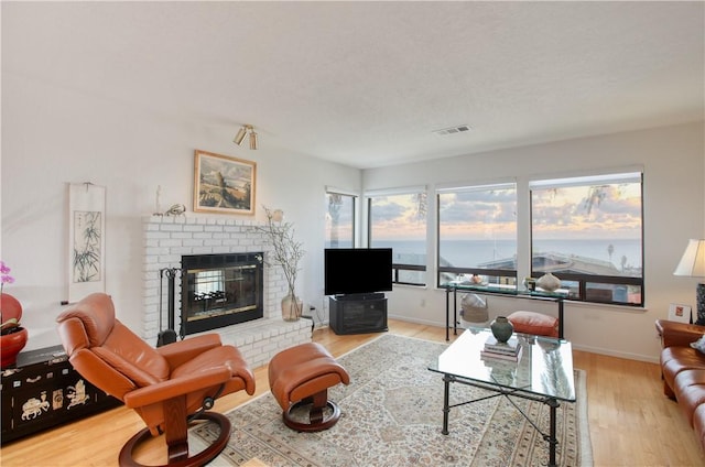 living room with baseboards, wood finished floors, visible vents, and a fireplace