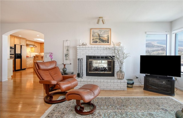 living area featuring arched walkways, light wood-style floors, and a fireplace