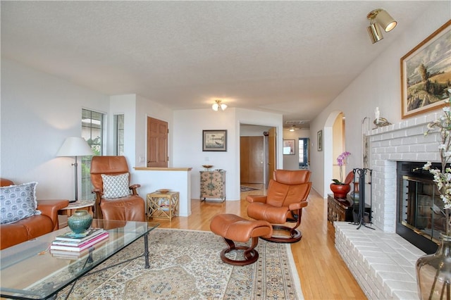 living area with arched walkways, a textured ceiling, wood finished floors, and a fireplace